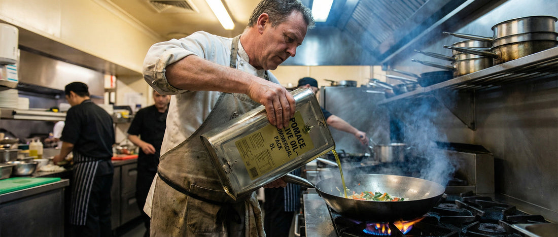 A professional chef pouring pomace olive oil into a hot pan for high-heat cooking in a commercial restaurant kitchen.